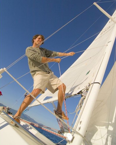 Low angle view of a young man standing on a sailboat and pulling a rope